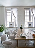 Gepolsterte Stühle mit weißem Überzug um Holztisch vor Sprossenfenster