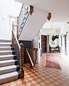 Foyer mit Teppichläufer auf Vintage Schachbrettmusterboden, seitlich Treppenaufgang, Geländer mit geschnitzten Holzpfosten