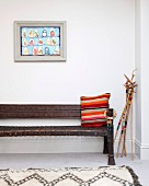 Striped cushion on antique bench next to decoratively painted walking sticks and below framed picture