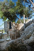 Outdoor shower behind stone wall and below olive tree growing on rocky slope