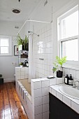 Washstand and bathtub with half-height, tiles partition walls and varnished wooden floor in bathroom of period apartment