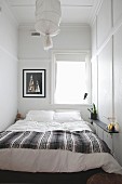 Double bed below window in narrow bedroom with simple, white-painted panelling on walls and ceiling