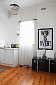 Poster with motto above vintage trunk next to window and simple kitchen counter in period apartment