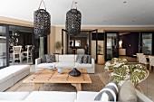 Sofa combination around wooden coffee table below dark, wicker, lantern-style lamps in spacious interior