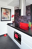 Kitchen counter with white base units, black worksurface and cylindrical, stainless steel extractor hood above cooker