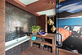 Bathtub next to washstand and brass pendant lamps in designer bathroom with mosaic tiles