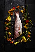 A whole raw fish surrounded by edible flowers (seen from above)