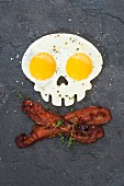 A skull-shaped fried egg with crispy bacon on a slate platter