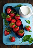 Fresh strawberries in a bowl and a jug of cream on a chopping board