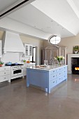 Island counter with blue drawer fronts and marble worksurface in elegant, country-house kitchen with grey resin floor