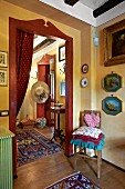 Cushions on chair below framed pictures on wall next to open doorway