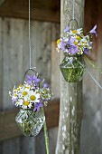 Romantische Wiesensträusschen aus Glockenblumen, Margeriten und Kamillenblüten in aufgehängten Glasvasen