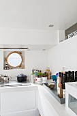 White kitchen counter with hob below porthole window of houseboat