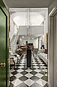 Blick durch offene Tür in elegantes Foyer mit Schachbrettmusterboden, oberhalb moderne Pendelleuchte