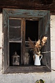 Enamel jug of dried flowers on windowsill of rustic wooden window