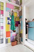 Colourful patchwork pattern on wall and view of woman in front of pale blue cabinet through open door