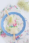 Home-made elderflower ice lollies on romantic floral plate on floral tablecloth