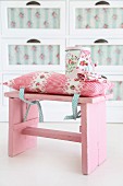Romantisches Stuhlkissen mit Rosenmuster und passender Blechdose auf rosafarbenem Vintage Schemel festgebunden