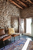 Brown leather chairs against stones wall and light falling on rug through open door in background