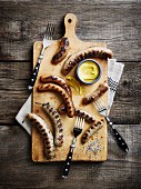 Various grilled sausages with mustard on a chopping board