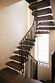 Winding metal staircase with wooden treads and handrail and tall stairwell window
