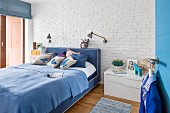 Double bed in shades of blue against whitewashed brick wall in bedroom