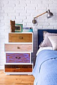 Tower of drawers with different fronts and handles as bedside cabinet against whitewashed brick wall