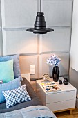 Black pendant lampshade above bedside cabinet against bedroom wall with panelled structure