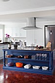 Blue-painted island counter with open-fronted shelved in modern, white fitted kitchen