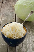 A bowl of sauerkraut with a fresh white cabbage in the background