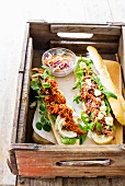 A pulled pork baguette with barbecue sauce, and a pulled pork baguette with mustard sauce and feta cheese in a wooden crate