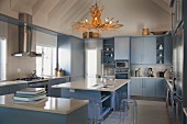 Modern kitchen with stone worksurfaces and pale blue cupboards; driftwood chandelier above island counter