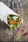 A wrap with falafel, pomegranate seeds, mint, cucumber, beetroot leaves and dill yoghurt