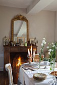 Festively set table in dining room with antique furniture and fire burning in open fireplace