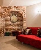 Red throw on sofa in cellar-like room with arched niche in brick wall
