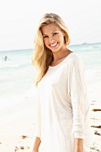 A young blonde woman on a beach wearing a long, white shirt