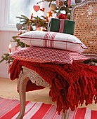 Woollen blanket, checked scatter cushions and gift on cane-back chair in front of Christmas tree