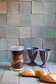 Stillleben mit antiken Trinkgefässen vor rustikal gefliester Küchenwand