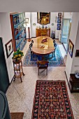 View down from gallery onto patterned rug and stone floor and dining area with antique, oval table in background in traditional interior