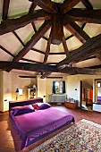 Violett bezogenes Doppelbett in grossem Schlafraum unter historischer, konzentrisch angelegter Holzbalkenkonstruktion