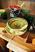 Place setting with painted ceramics and green beakers on rustic wooden table