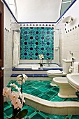 Luxurious bathroom with curved step, green floor tiles, fitted bathtub and blue and green floral wall tiles (Hotel Villa Cimbrone)