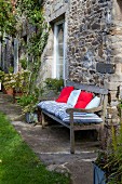 Cushions on wooden garden bench against façade of stone house