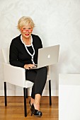 An older business woman sitting in an armchair with a laptop