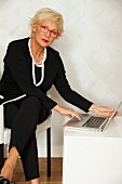 Ältere Businessfrau sitzt in Sessel neben Laptop