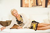 An elegantly dressed older woman lying on a white sofa