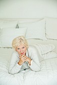 An older woman wearing white pyjamas and a cardigan lying on a bed