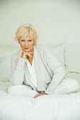 An older woman wearing white pyjamas and a cardigan lying on a bed