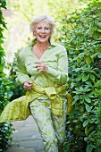 An older woman wearing a light green blouse and green-and-white trousers running in a garden