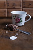 A used tea bag on a spoon and a tea cup with an Eat Frisian tea rose pattern